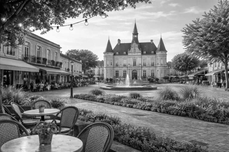 Place du centre de Talence avec architecture locale, fontaine et terrasses de cafés dans une ambiance calme et ensoleillée, sans personnes visibles.