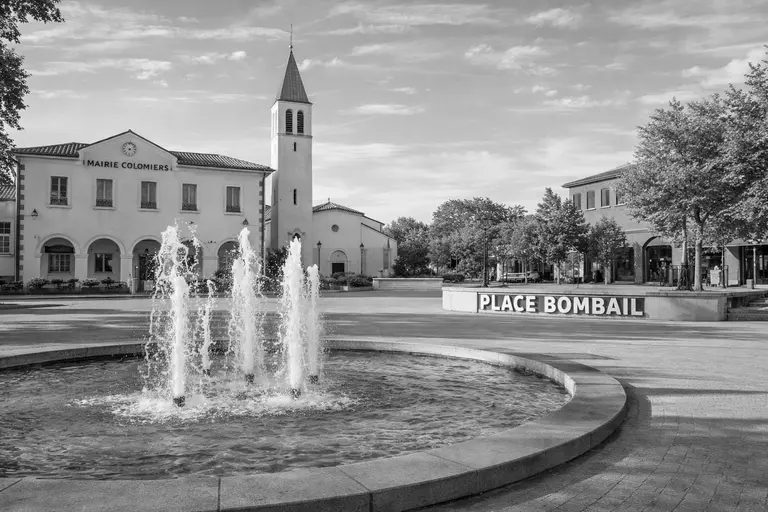 Place Bombail à Colomiers avec fontaine centrale, mairie et église en arrière-plan dans une grande place piétonne sans personnes visibles.