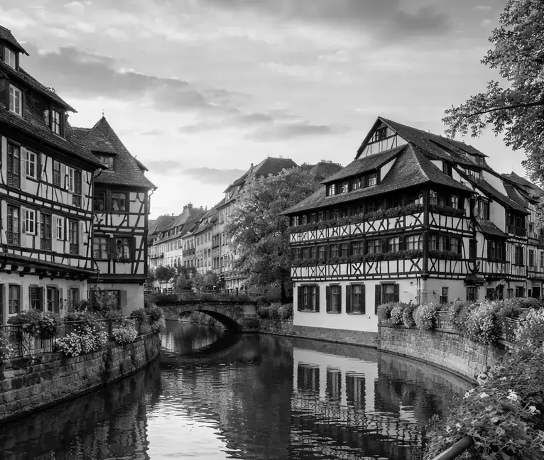 Maisons à colombages traditionnelles bordant un canal dans le quartier de la Petite France à Strasbourg au coucher du soleil, avec un petit pont et une promenade pavée