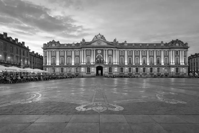 Place du Capitole à Toulouse avec le bâtiment historique illuminé au coucher du soleil, grande place pavée et architecture typique de la ville rose